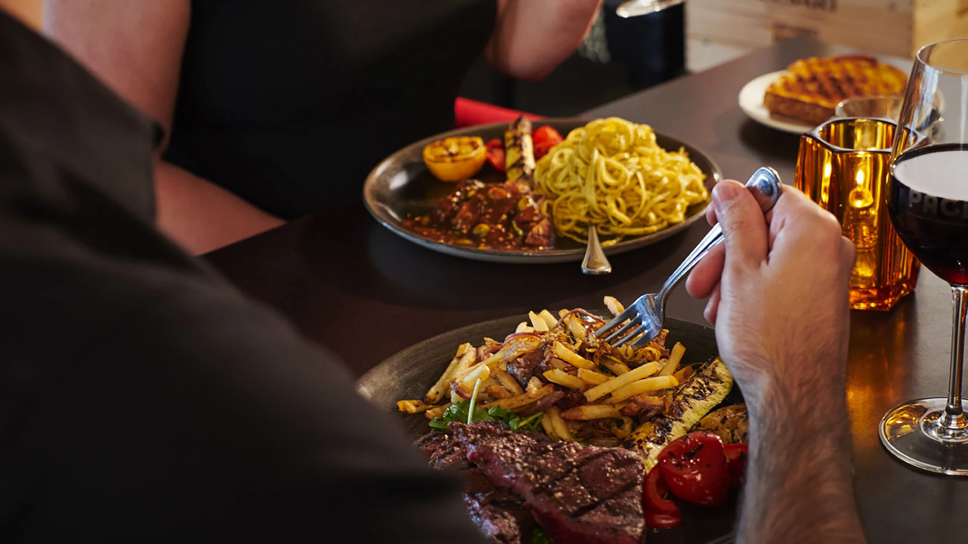 Guests enjoying an Italian meal with grilled steak, roasted vegetables, fries, and pasta at PACINI.