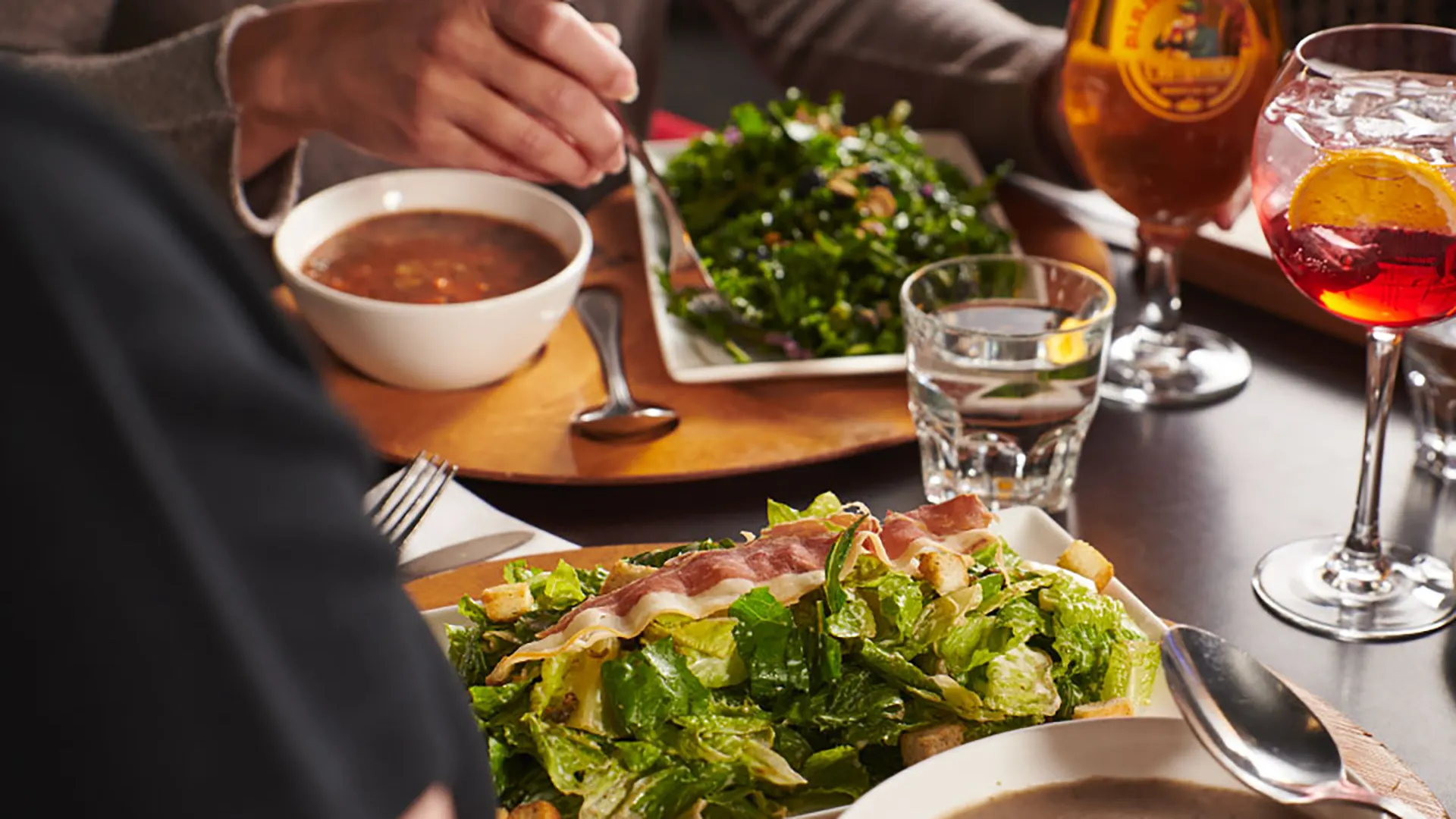 Guests sharing a meal with fresh salad, homemade soup, and beverages in the welcoming atmosphere of PACINI.