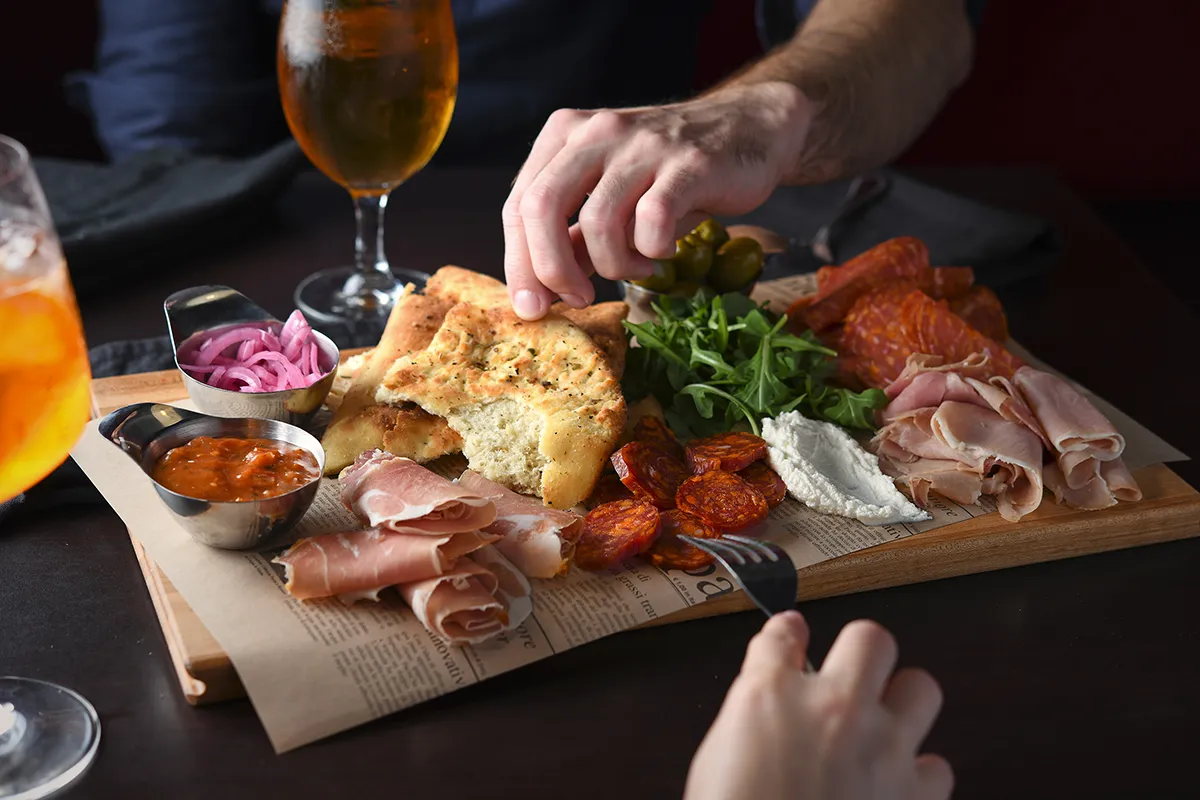 Italian antipasti board featuring cured meats, focaccia bread, creamy ricotta, marinated vegetables, and drinks served at PACINI.