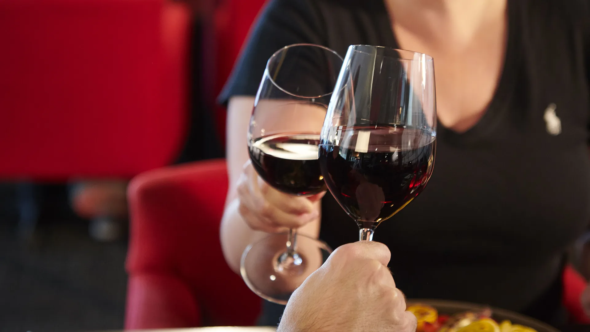 Two people clinking glasses of red wine in the warm and welcoming atmosphere of a PACINI restaurant.
